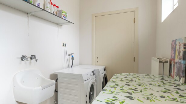 A laundry room with a washing machine, a sink, and a shelf with cleaning supplies. - Villa Jules (Holsbeek)