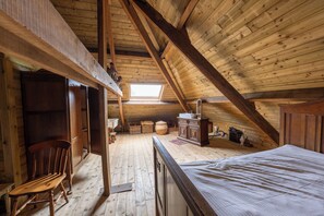 A high-ceilinged attic bedroom with a sloped roof, wooden beams, a skylight, a bed, a dresser, and a chair. - Villa Jules (Holsbeek)