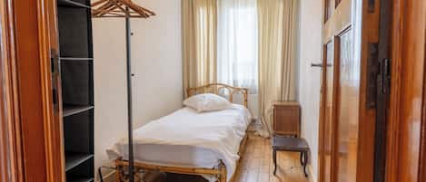 A single bed with a wooden frame, a small bedside table, and a wardrobe with a metal rack.