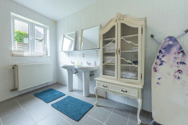 A bathroom with a white radiator, two sinks, a cabinet with glass doors, and a blue rug on the floor. - Villa Jules (Holsbeek)