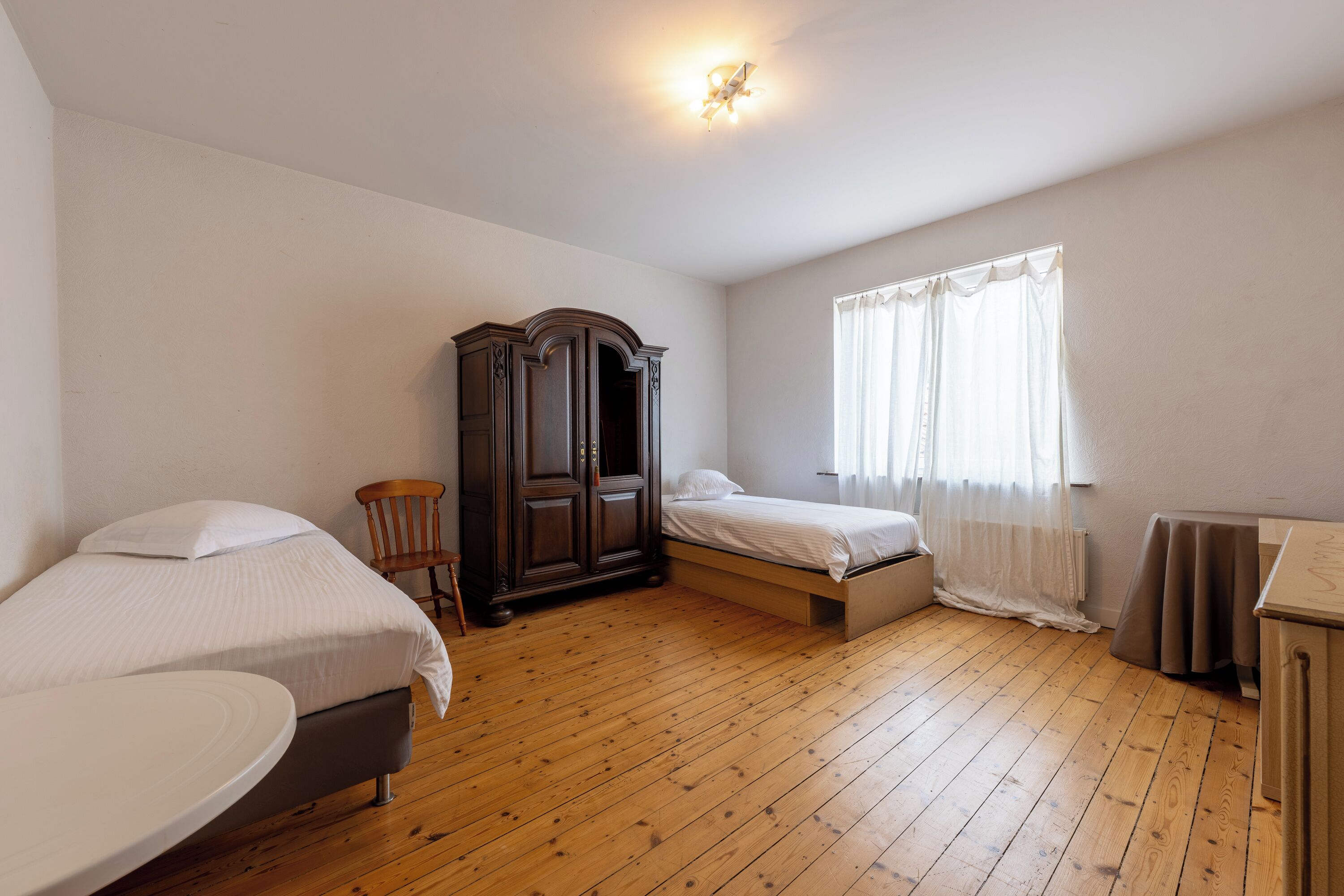 Une chambre avec deux lits, une armoire en bois, une chaise et une petite table.