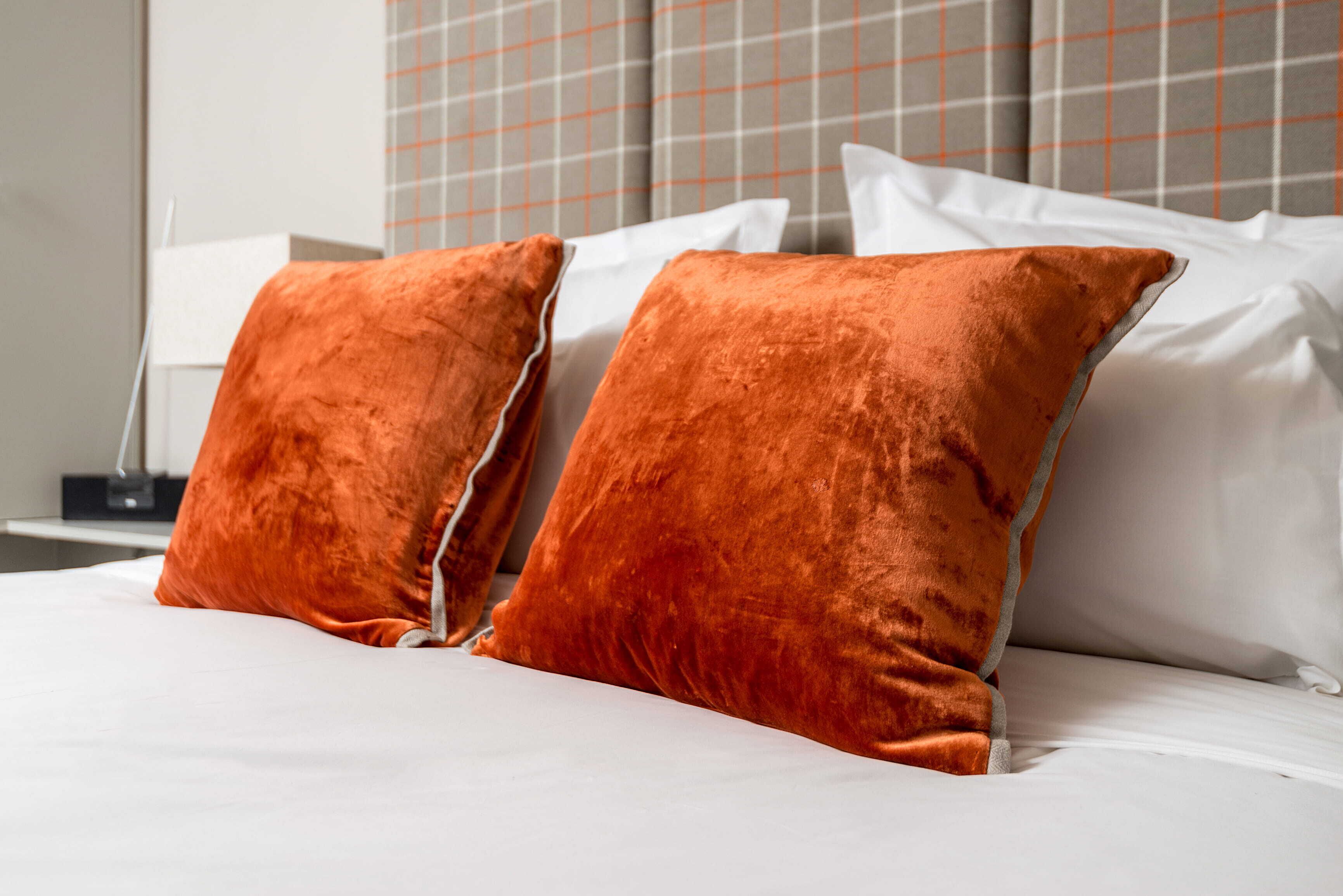 A bed with white linens and two orange pillows.