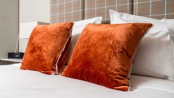 A bed with white linens and two orange pillows.