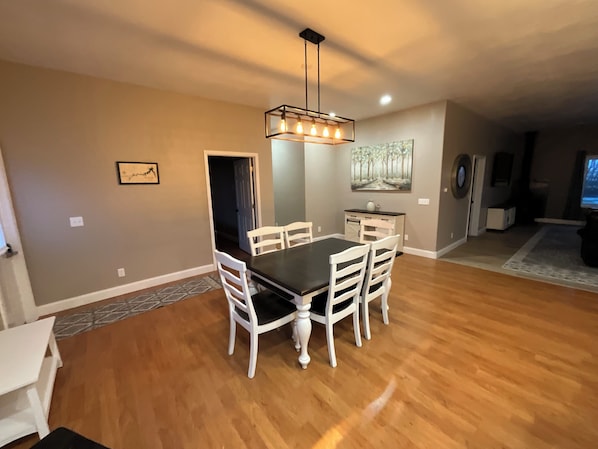 A dining area with a rectangular table, white chairs, a chandelier, and a painting on the wall.