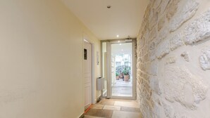 A hallway with a stone wall, a door, and a view of a garden through a glass door. - Spacious studio, chic and quiet, attractive Bon Marché district (Paris)
