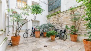 A courtyard with potted plants, bicycles, and a stone wall. - Spacious studio, chic and quiet, attractive Bon Marché district (Paris)