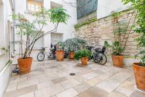 A courtyard with potted plants, bicycles, and a stone wall. - Spacious studio, chic and quiet, attractive Bon Marché district (Paris)