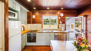 Une cuisine dotée de meubles en bois, d’un four à micro-ondes, d’un four traditionnel et d’un lave-vaisselle. Une fenêtre offre une vue sur la verdure environnante.