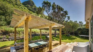 Une pergola en bois avec une table et des chaises, un barbecue et un espace patio offrant une vue sur un paysage montagneux.
