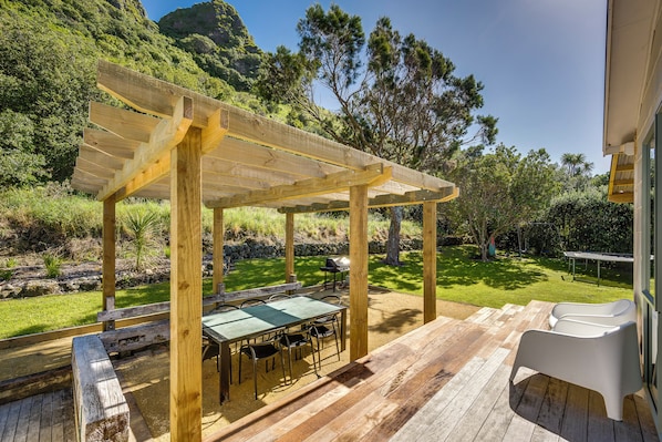 Una pérgola de madera con una mesa, sillas, una parrilla y un patio con vistas a un paisaje montañoso.