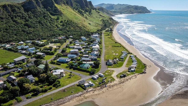 Vue aérienne d’une zone résidentielle côtière, avec des maisons, une plage et des montagnes.
