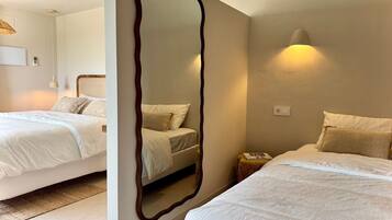 A hotel room with two beds, a large mirror, a bedside table, a lamp, and a wall-mounted light fixture.