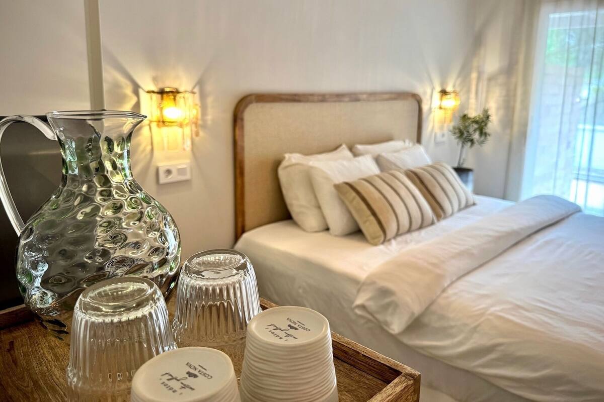 Ein Hotelzimmer mit einem Bett, Kissen, einem Nachttisch mit einem Glasbehälter und Kerzenhaltern sowie Wandleuchten.