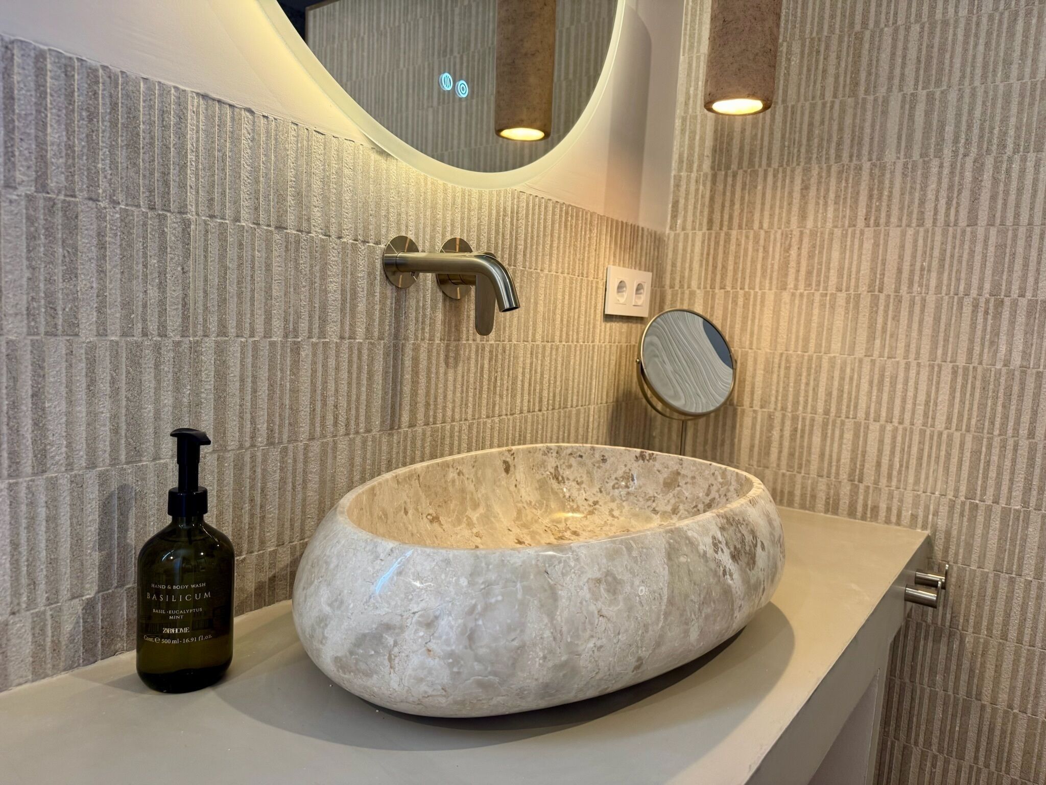 A bathroom with a stone sink, a hand and body wash bottle, a mirror, and a towel rack.