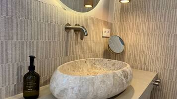 A bathroom with a stone sink, a hand and body wash bottle, a mirror, and a towel rack.
