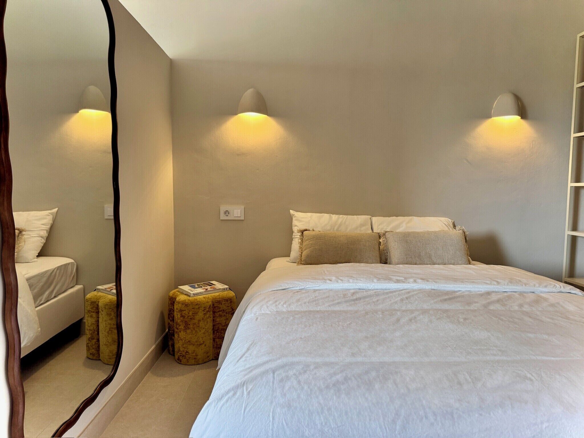 Une chambre à coucher avec un lit, deux lampes de chevet, un miroir, un petit tabouret et une échelle appuyée contre le mur.