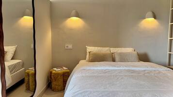 Une chambre à coucher avec un lit, deux lampes de chevet, un miroir, un petit tabouret et une échelle appuyée contre le mur.