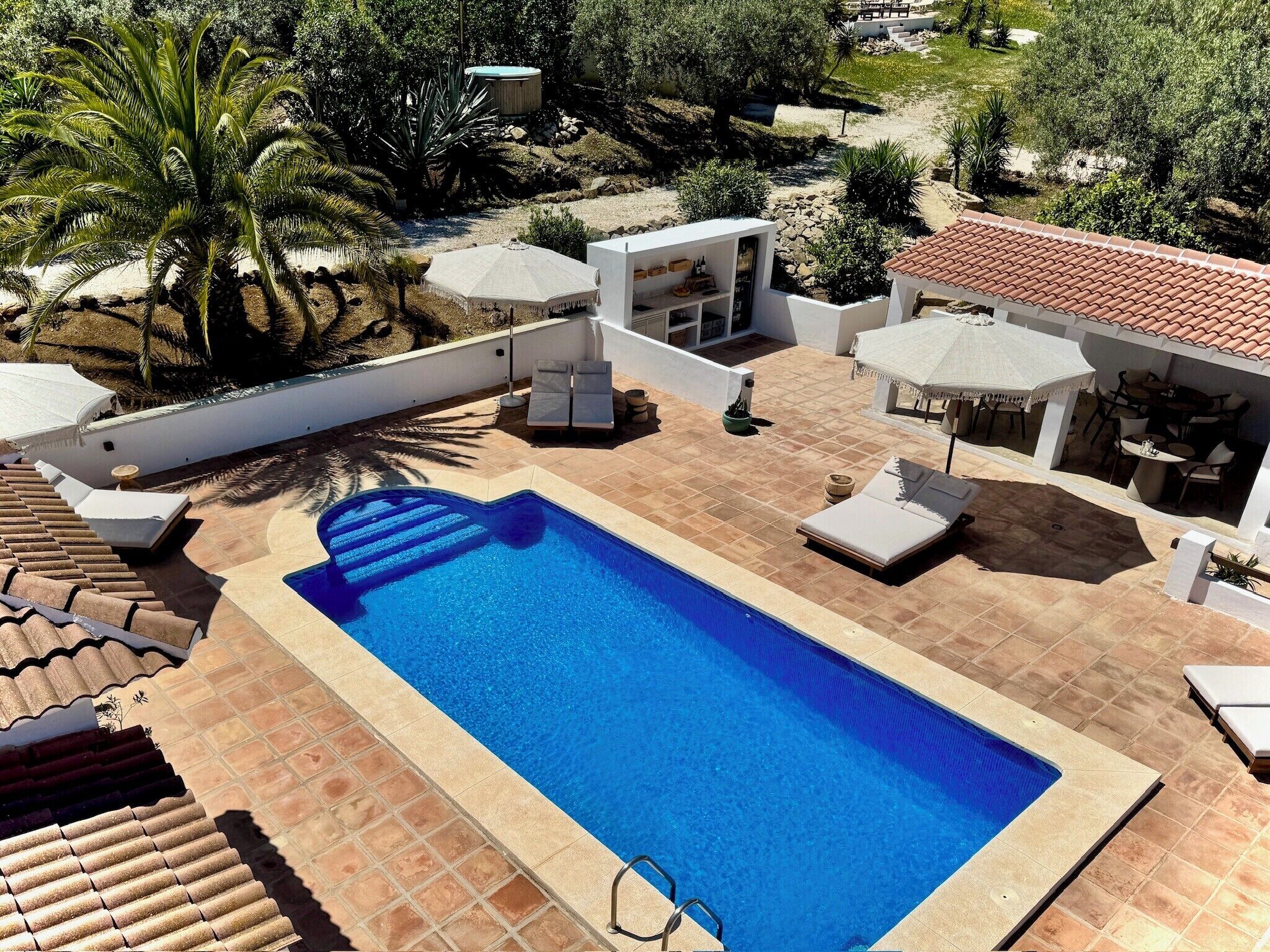 Une piscine avec des chaises longues, un petit coin bar et une terrasse avec des sièges extérieurs.