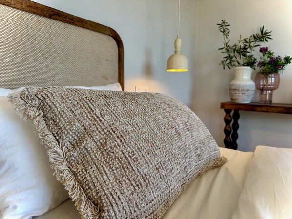 A bed with a textured blanket, a wooden headboard, a hanging light fixture, and a shelf with decorative items. - Vida Lenta Boutique Finca (Álora)