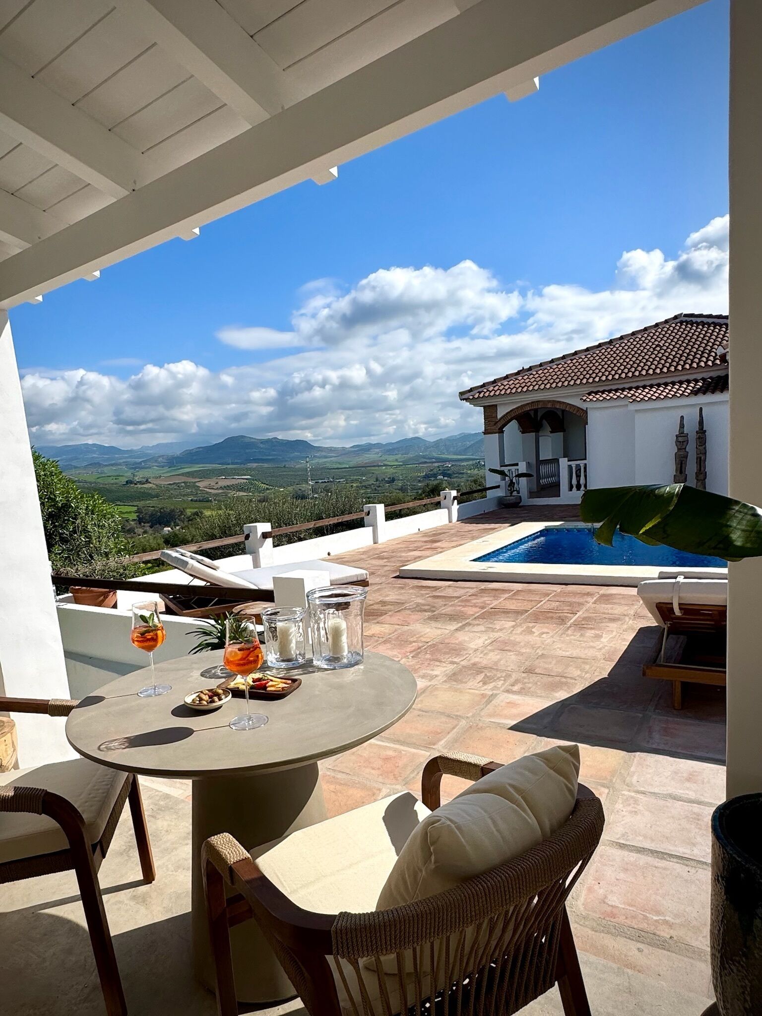 Une terrasse avec une table dressée pour deux personnes, une piscine et une vue sur les montagnes lointaines.