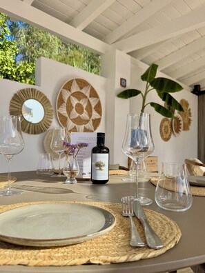 Una mesa de comedor dispuesta con platos, cubiertos y copas de vino, junto con una botella de vino y decoración en la pared.