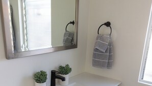 Ein Badezimmer mit einem weißen Waschbecken, einem Spiegel, zwei Topfpflanzen und einem Handtuchhalter mit Handtüchern.