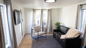 Ein modernes Wohnzimmer mit einer Couch, einem Sessel, einem Fernseher und einer Pflanze.