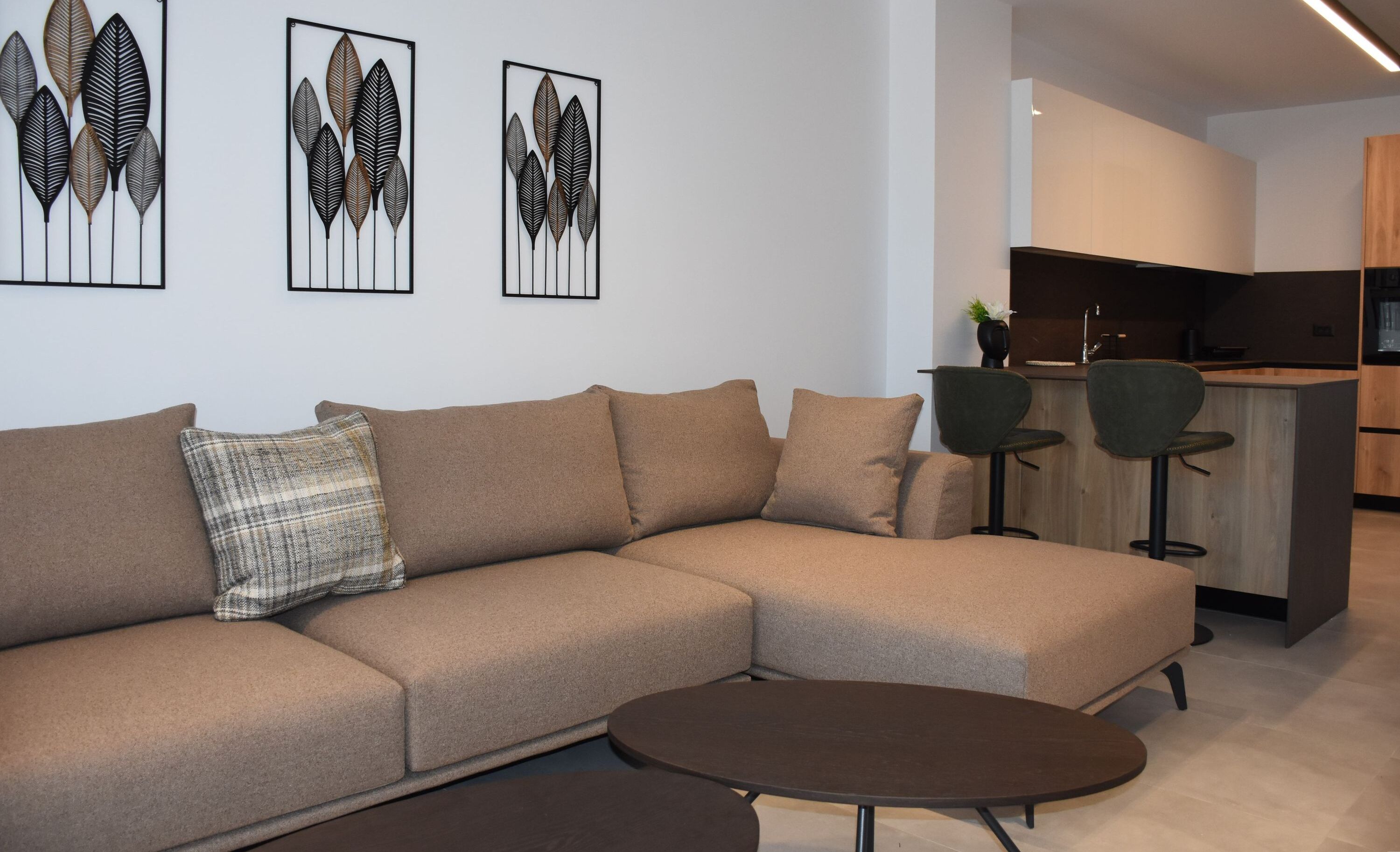 A modern living room with a sectional sofa, a round coffee table, and a kitchen area in the background.