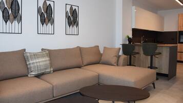 A modern living room with a sectional sofa, a round coffee table, and a kitchen area in the background.