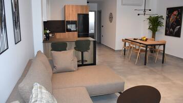 A modern living room with a sofa, a dining table with chairs, and a kitchen in the background.