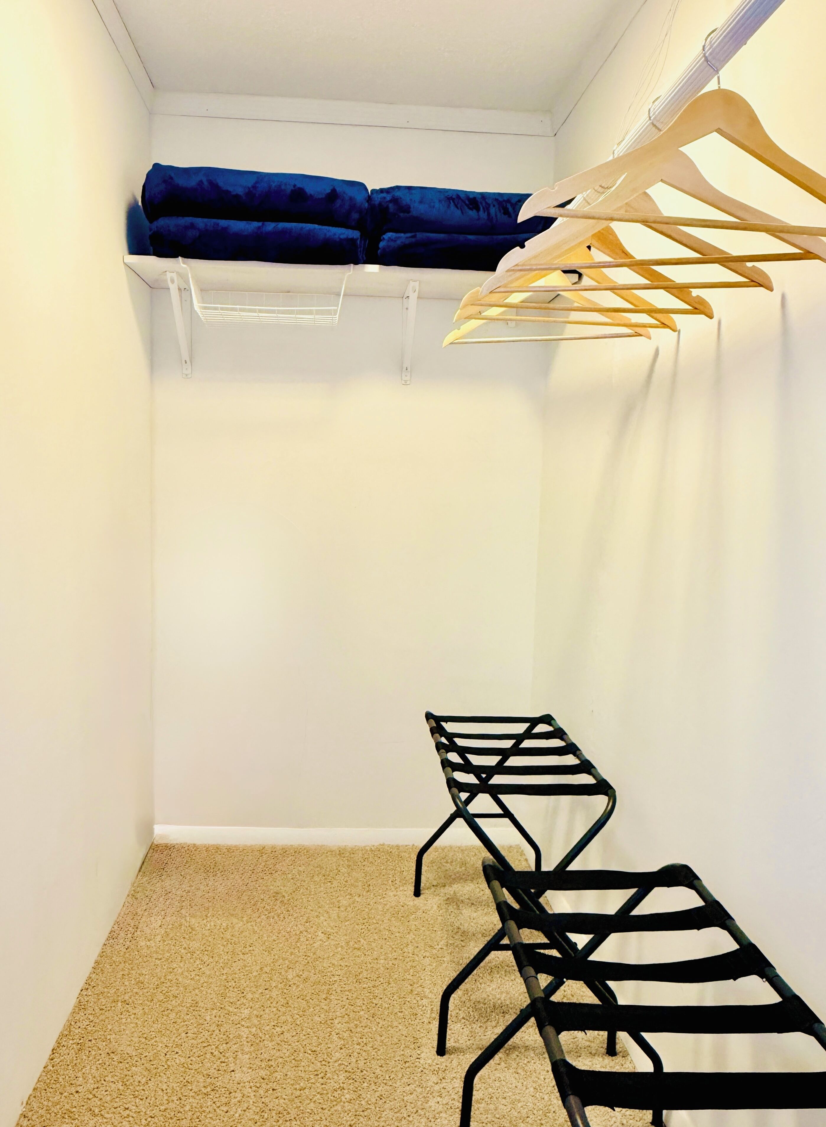 A small, well-organized closet with a hanging rack, a bench, and a shelf.
