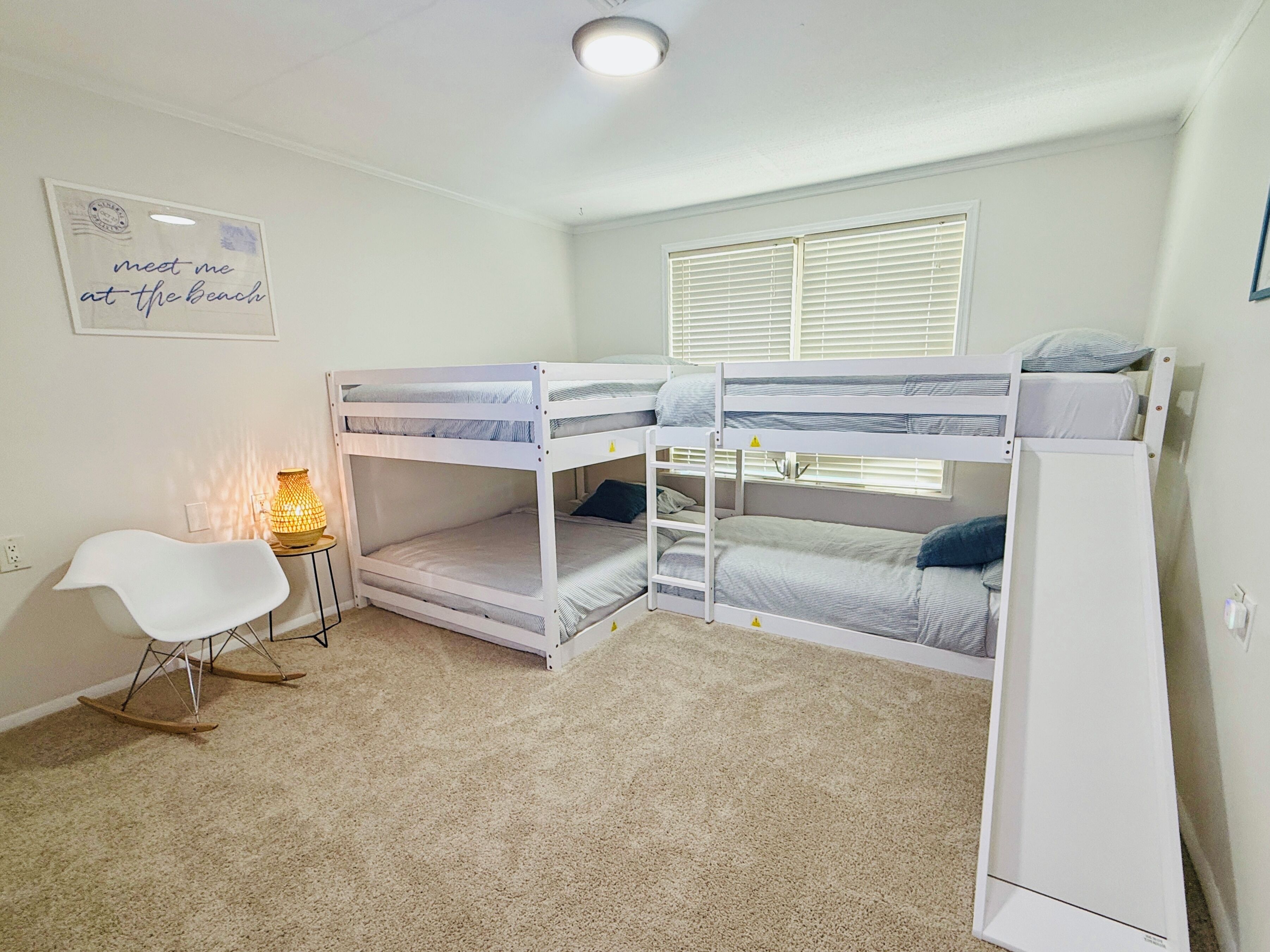 A bunk bed room with a desk, chair, and a lamp.