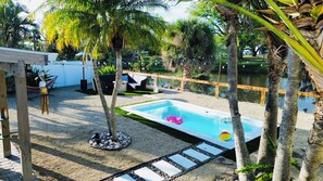 Une piscine avec un flotteur circulaire, entourée de palmiers et dotée d’une terrasse en bois.