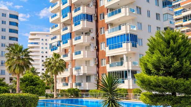 A multi-story hotel with balconies, a swimming pool, and palm trees. - LOVELY  RESİDENCE 2+1 CLOSE TO SEA WİTH POOL (mahmutlar)
