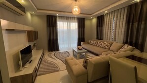 A modern living room with a flat-screen TV, sofa, coffee table, and decorative rug. - LOVELY  RESİDENCE 2+1 CLOSE TO SEA WİTH POOL (mahmutlar)