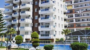 A multi-story hotel with balconies, a swimming pool, and a clear blue sky. - LOVELY  RESİDENCE 2+1 CLOSE TO SEA WİTH POOL (mahmutlar)