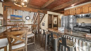 Una cocina rústica con vigas de madera, una chimenea de piedra y una zona de bar con taburetes.