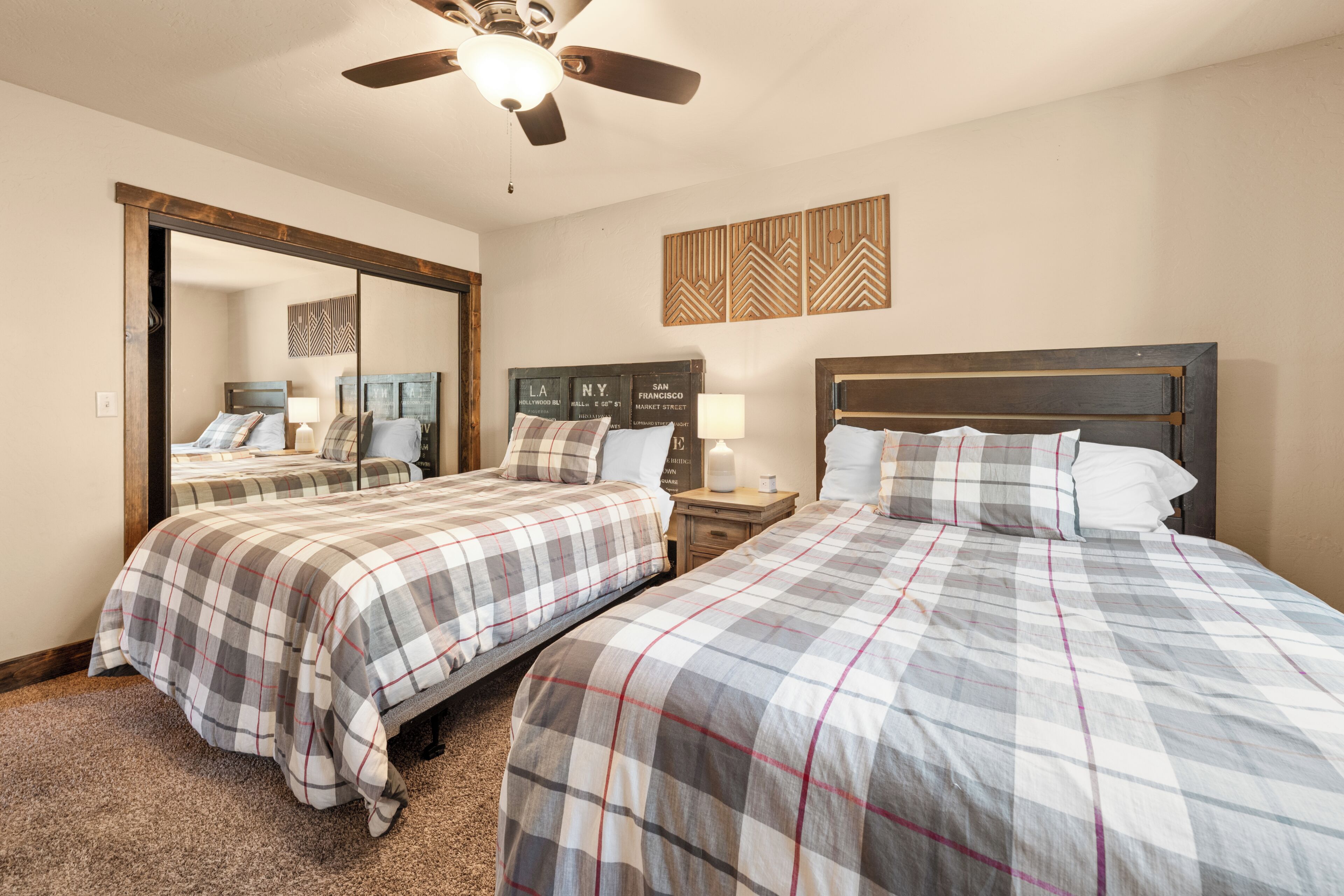 A hotel room with two beds, a ceiling fan, a mirror, and a wall with city names.