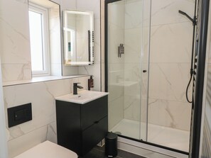 Een moderne badkamer met een douchecabine van glas, een wit wastafelmeubel en een donkere badkamerkast.