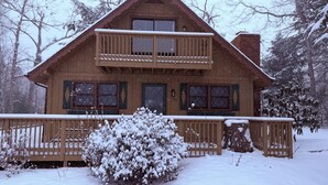 A two-story wooden cabin with a balcony, surrounded by snow-covered trees. - The Cozy Chalet (Asheville)