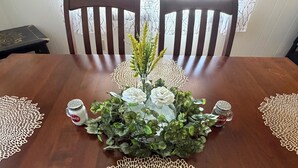 A dining table with a centerpiece of white flowers and greenery, surrounded by two salt and pepper shakers, and two doilies on the tablecloth. - The Cozy Chalet (Asheville)