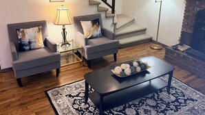 A living room with two grey armchairs, a black coffee table, a patterned rug, a staircase, and a fireplace. - The Cozy Chalet (Asheville)
