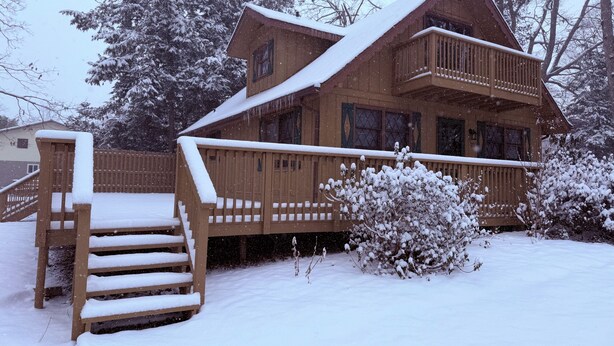 A wooden cabin with a balcony, a staircase, and a snow-covered landscape. - The Cozy Chalet (Asheville)