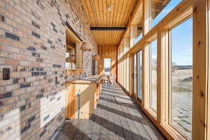 A long, narrow corridor with wooden walls and large windows, leading to a kitchen area with a sink and a dining table.