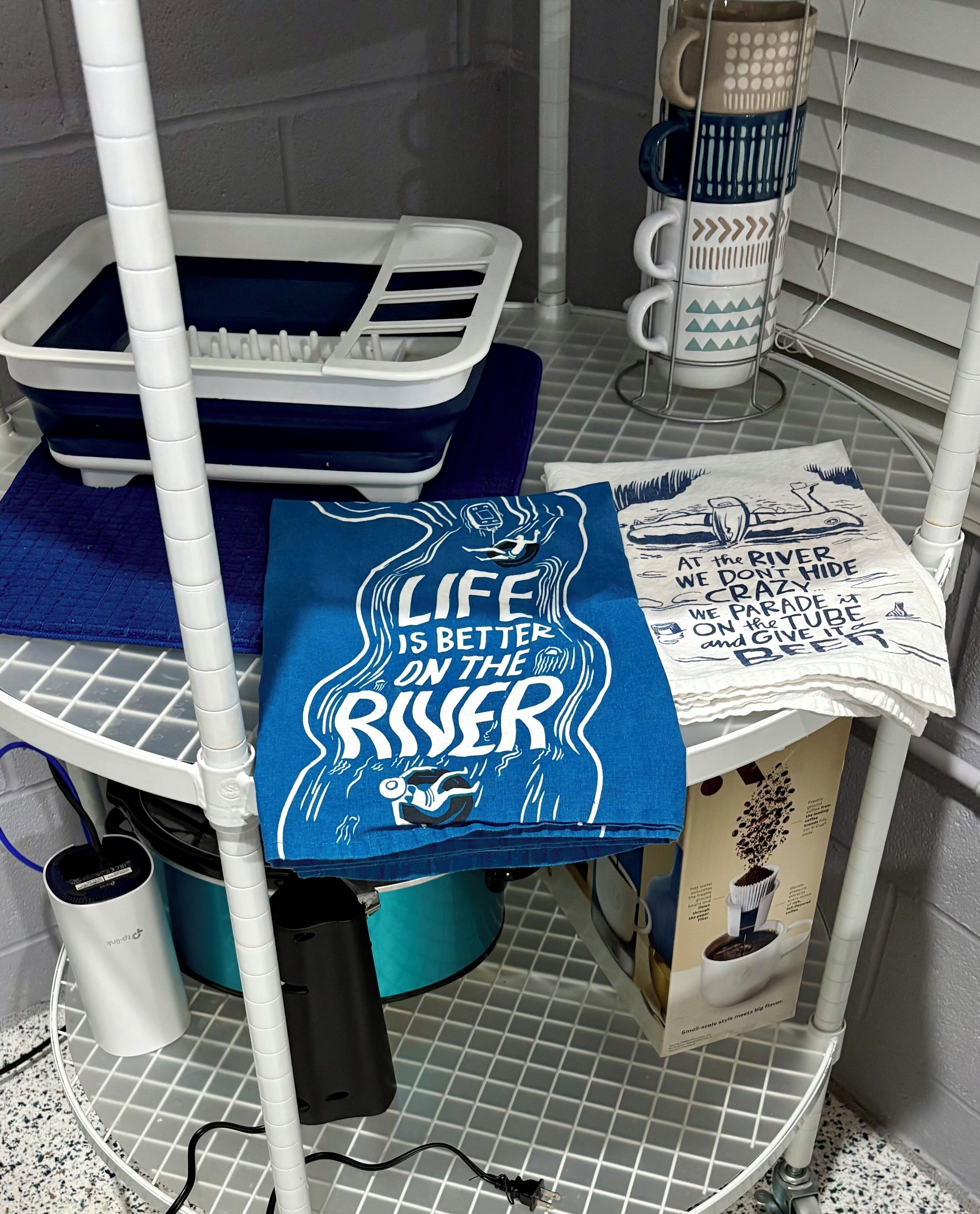 A bathroom with a shower area, a towel rack, a coffee maker, and a towel with a motivational quote.