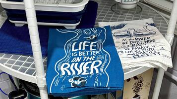 A bathroom with a shower area, a towel rack, a coffee maker, and a towel with a motivational quote.