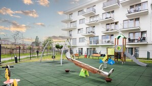 Un’area giochi con altalene, una bilancia e uno scivolo, circondata da un edificio con balconi.