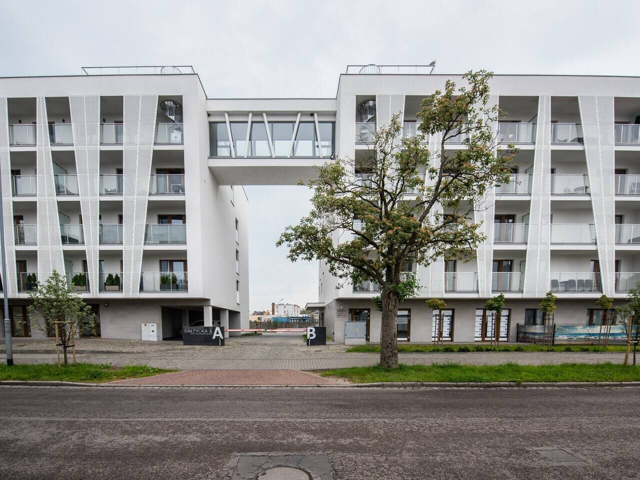 A modern building with a central atrium, multiple balconies, and a tree in the foreground.