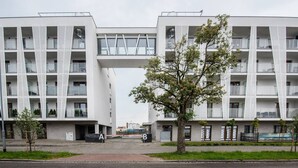Un edificio moderno con un atrio centrale, numerosi balconi e un albero in primo piano.