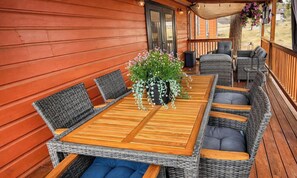 A covered outdoor seating area with a wooden table and wicker chairs, a potted plant, and a view of the outdoors. - Canava Cabin | 3BR + Private Casita • Pool Table (Ruidoso)